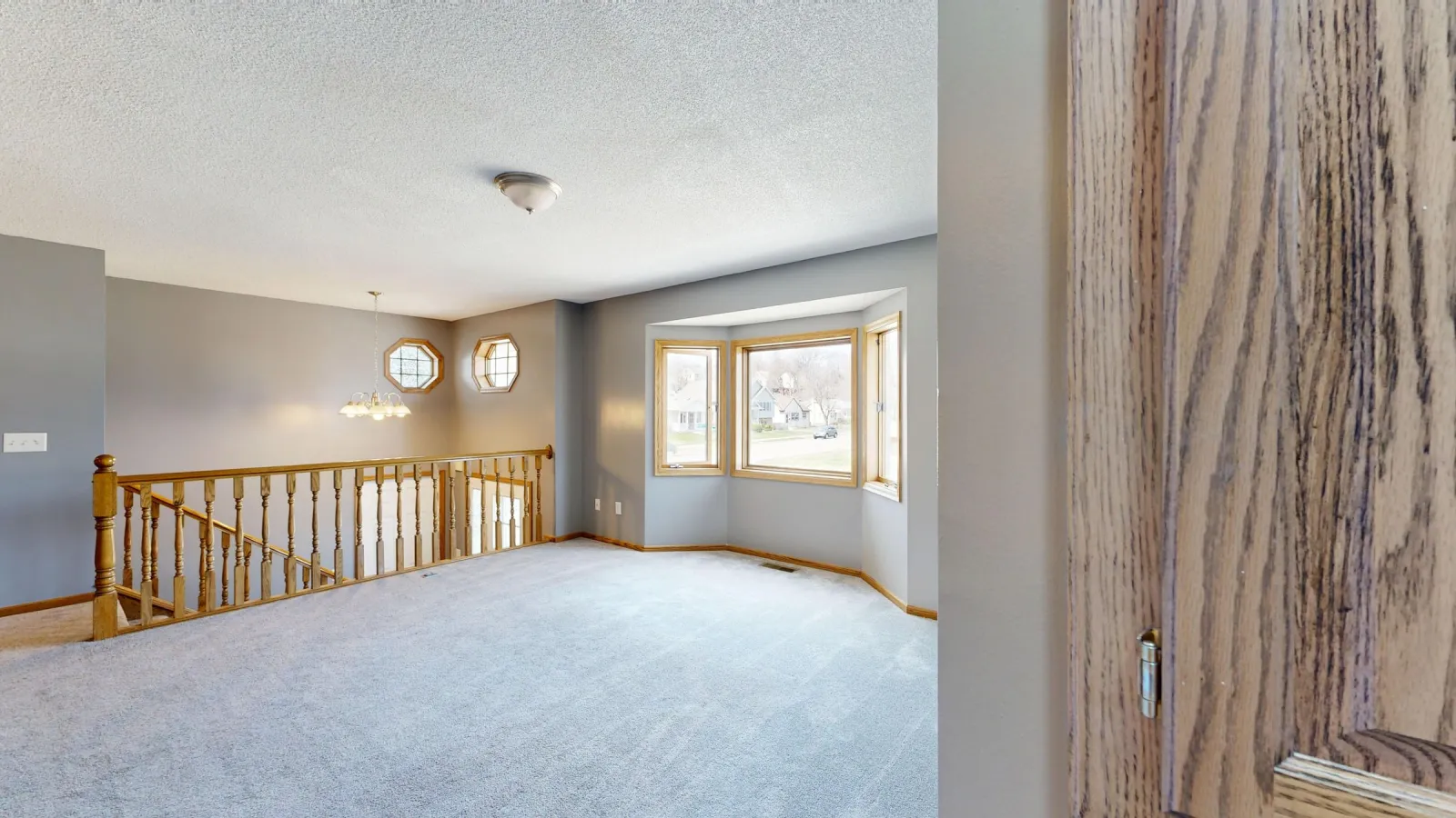 Carpet in an upstairs room with a bay window and wood stair railing